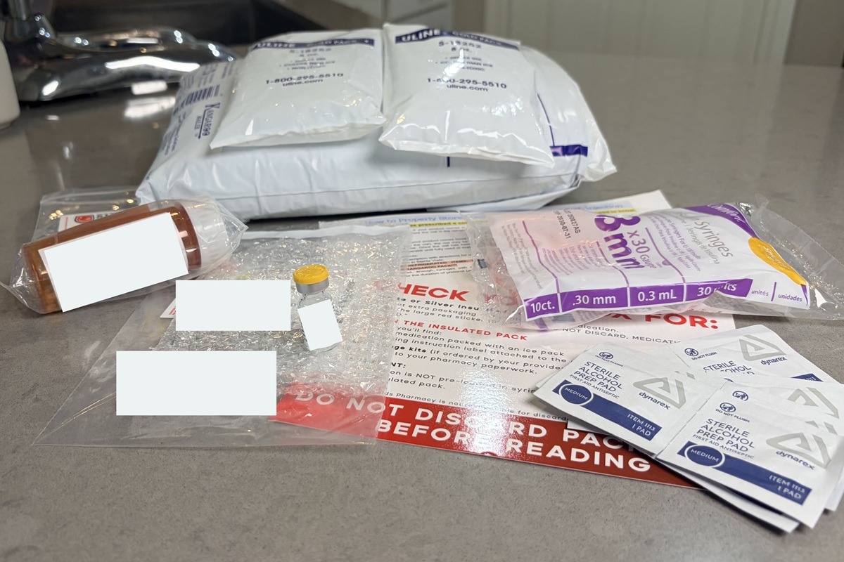 All Henry Meds materials, including two large ice packs on a protective package, alcohol wipes, extra sharps, instructions, and a medication vial alongside nausea pills