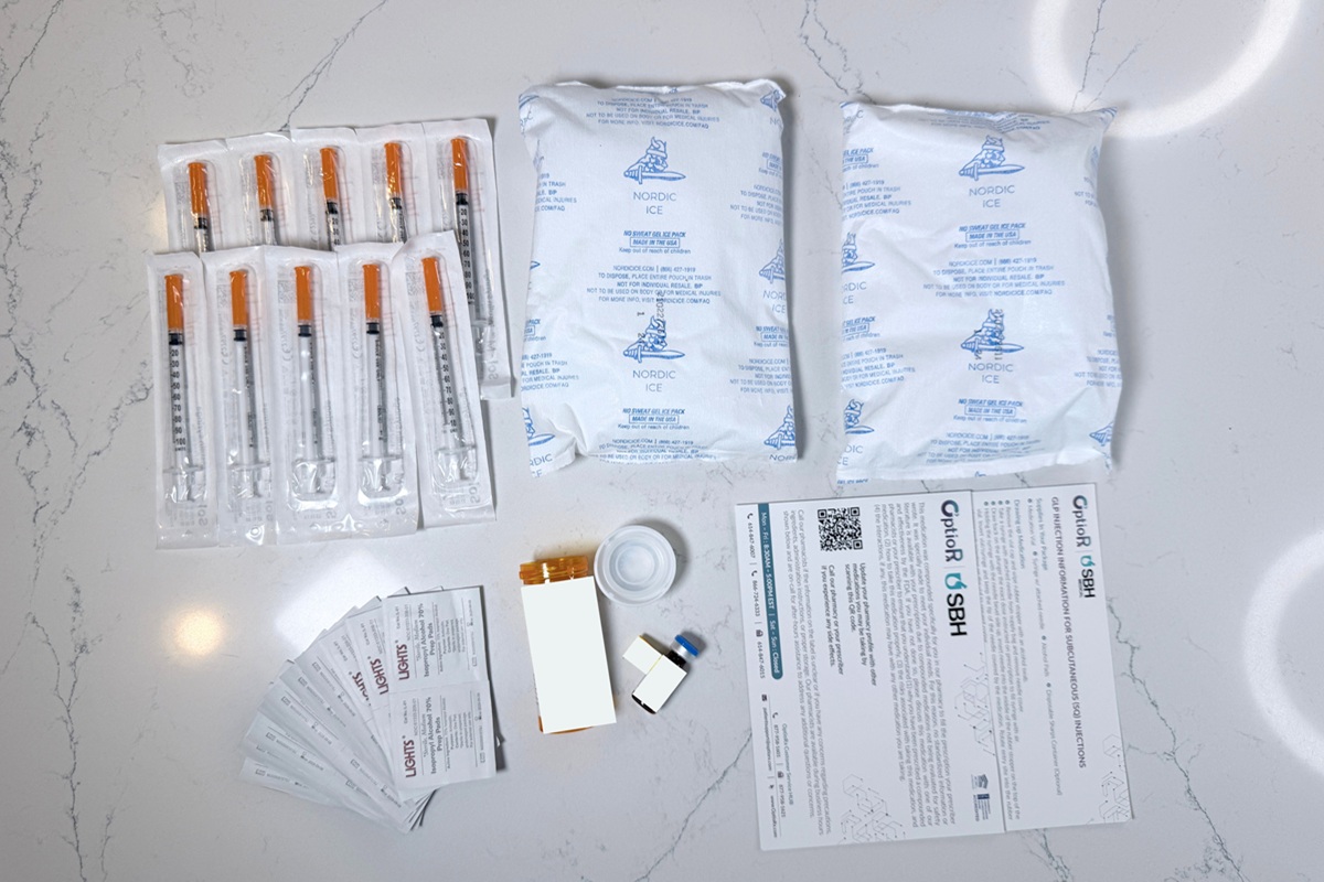 All Pomegranate materials spread out on a table, including two large ice packs, extra sharps, alcohol wipes, instructions, and a medication vial next to the pill bottle it came in